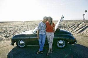 An older couple on a beach date sporting an older car and surfboard