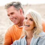 Mature man and woman sitting on the beach and laughing.