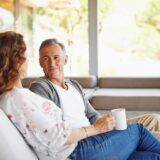 A couple sitting on the couch talking over coffee.