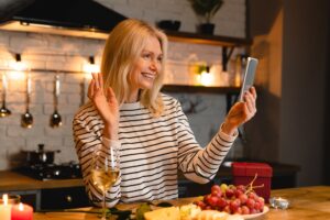 Blonde woman in a upscale kitchen smiling and waving into her phone.